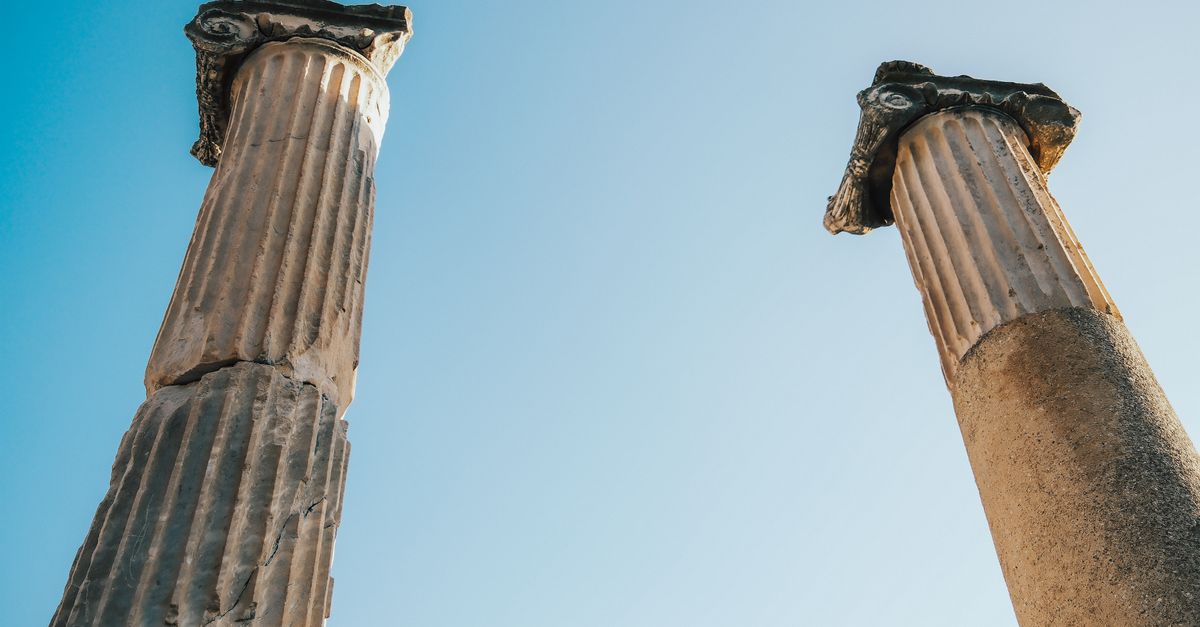 Two ancient Greek columns stand under a bright clear blue sky, showcasing historical architecture.